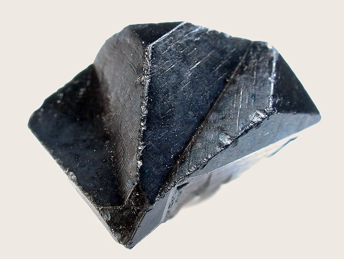 Black thorianite penetration twin crystal with sharp cube faces on a pale background