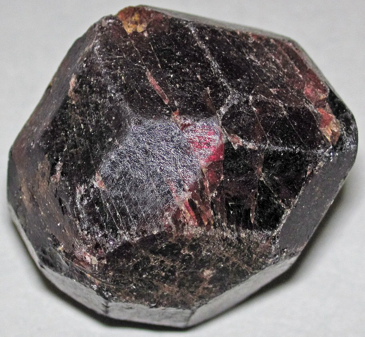 Dark red almandine garnet crystal with many flat faces on a white background
