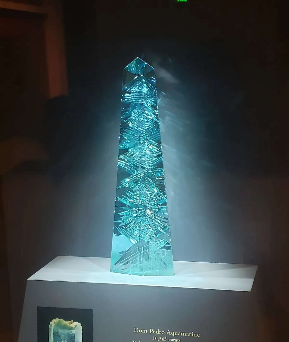 Tall blue green Dom Pedro aquamarine obelisk with carved facets lit on a museum pedestal